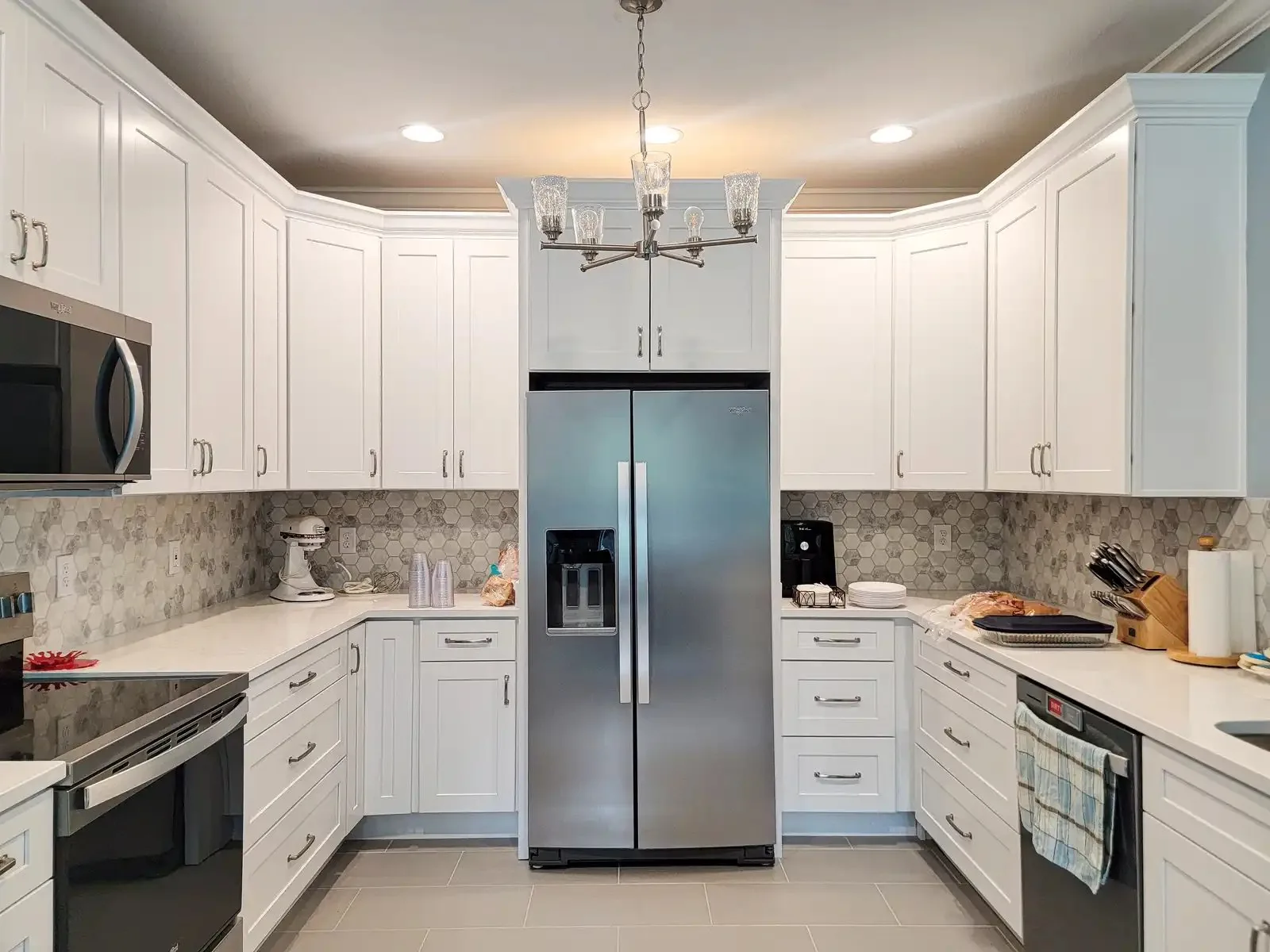A remodeled kitchen with white shaker cabinetry, a marble hex tile backsplash, and a chandelier