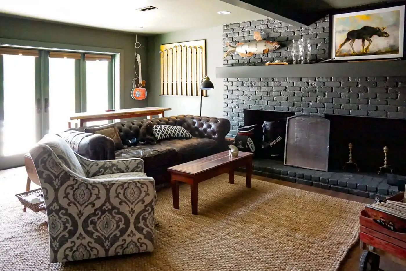 A remodeled living room with a painted brick fireplace, a leather chesterfield sofa, and a jute rug
