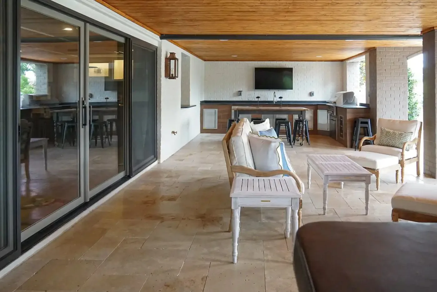 A covered outdoor living area with a wood plank ceiling, built-in grill, and bar seating