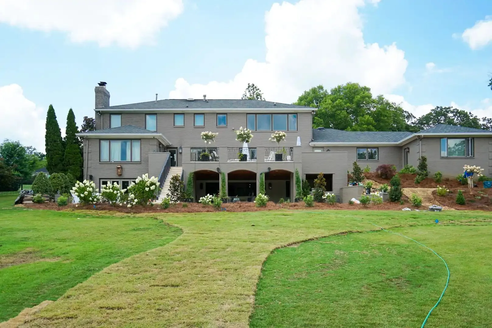 The rear elevation of a remodeled brick home with new landscaping and a covered lower terrace