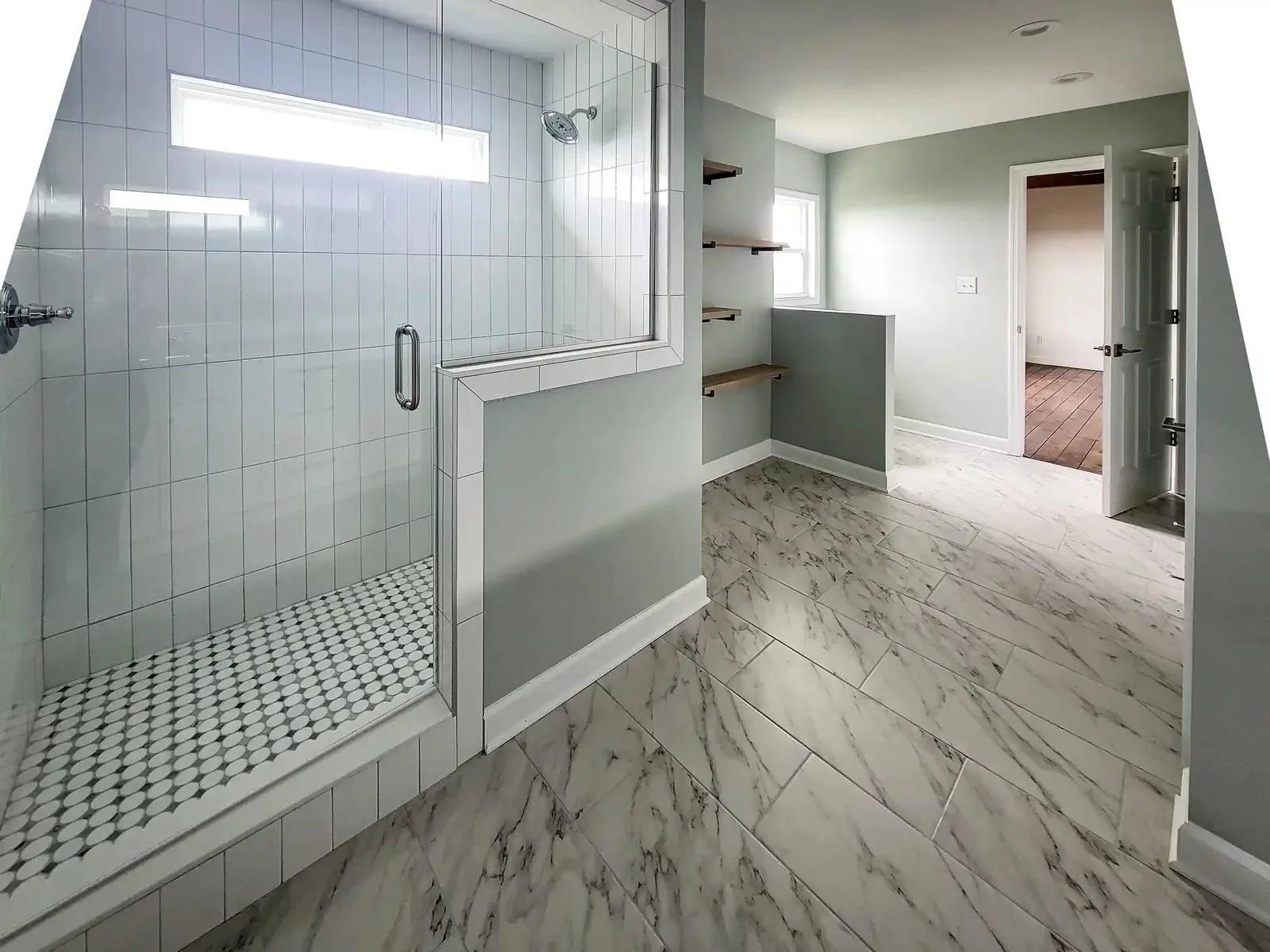 A remodeled bathroom with a tiled walk-in shower, marble tile floor, and open wood shelving
