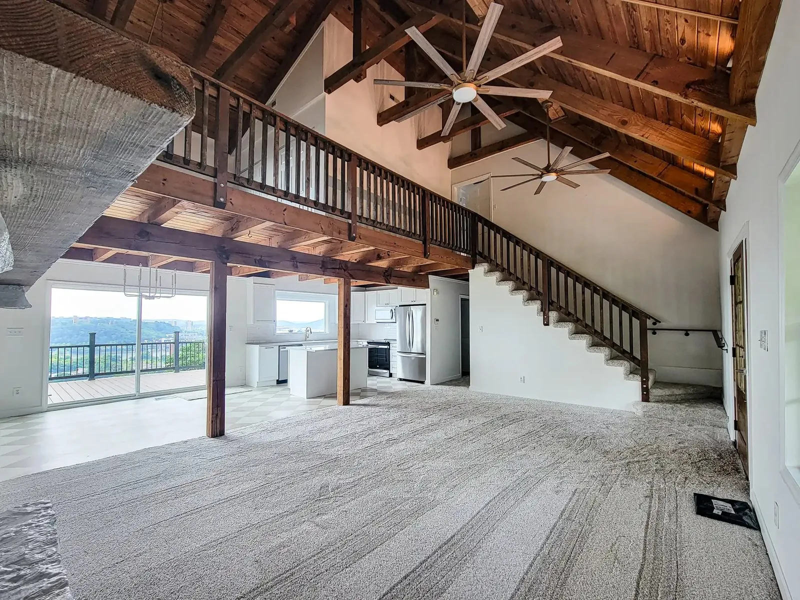 An open great room under exposed timber beams, with a loft above and a kitchen beyond