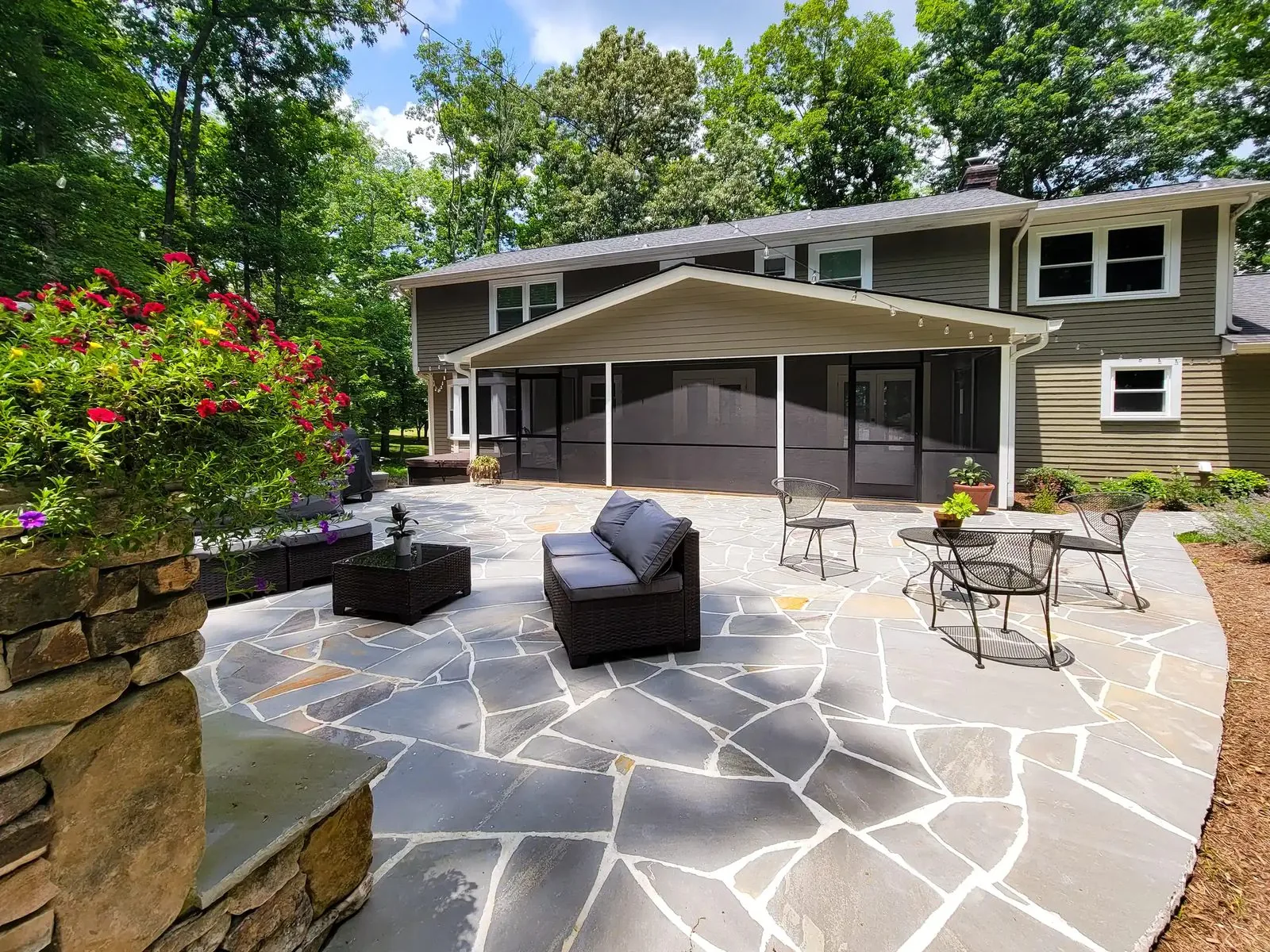 A flagstone patio and screened porch at the back of a home